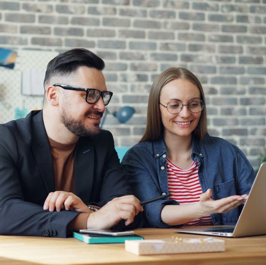 a man and a woman sitting at a table looking at a laptop