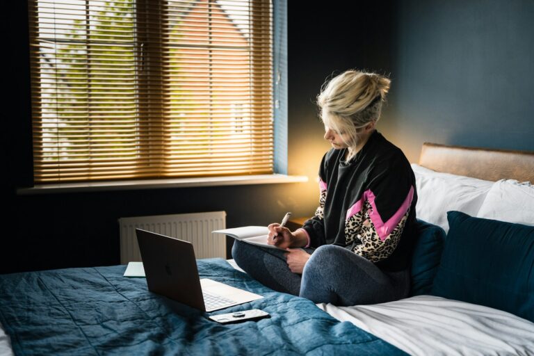 woman in purple and white floral long sleeve shirt and gray pants sitting on bed